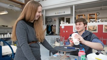 Carla Collins smiles as a student as he applies glaze to a ceramic mug