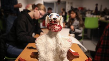 A dog puppet on a table with students working in the background.